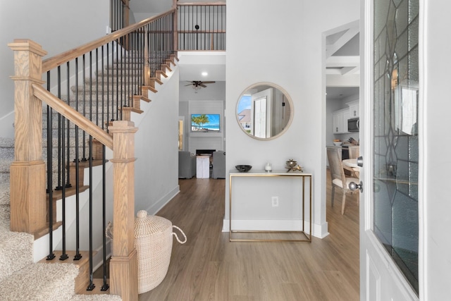 entryway with a towering ceiling, ceiling fan, and wood-type flooring