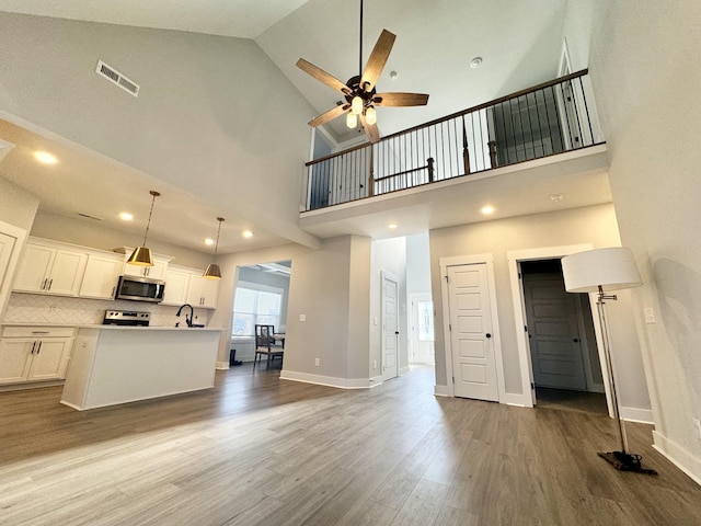 unfurnished living room with light wood-type flooring, high vaulted ceiling, ceiling fan, and sink