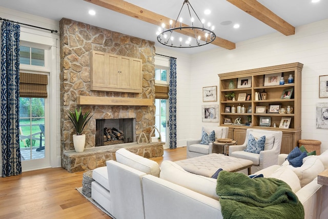 living room featuring a notable chandelier, beam ceiling, light hardwood / wood-style floors, and a stone fireplace