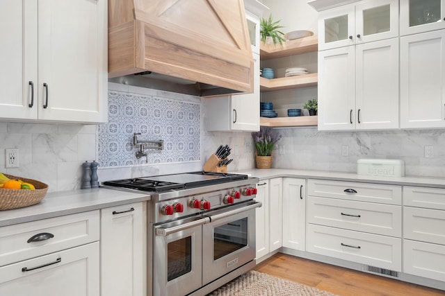 kitchen featuring custom exhaust hood, double oven range, light hardwood / wood-style floors, backsplash, and white cabinets