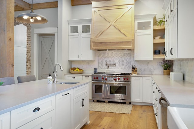 kitchen featuring range with two ovens, hanging light fixtures, backsplash, white cabinetry, and sink