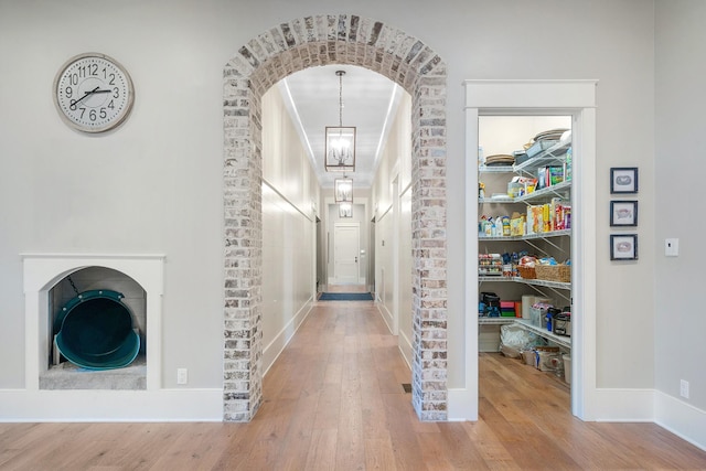 hallway featuring brick wall, hardwood / wood-style floors, and a notable chandelier