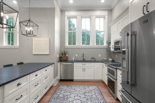 kitchen with stainless steel appliances, sink, decorative light fixtures, white cabinetry, and a chandelier