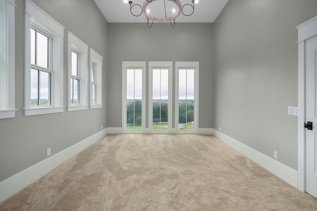 empty room with an inviting chandelier, light colored carpet, and plenty of natural light