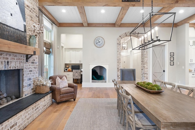 dining space featuring a brick fireplace, a notable chandelier, light hardwood / wood-style floors, and beamed ceiling