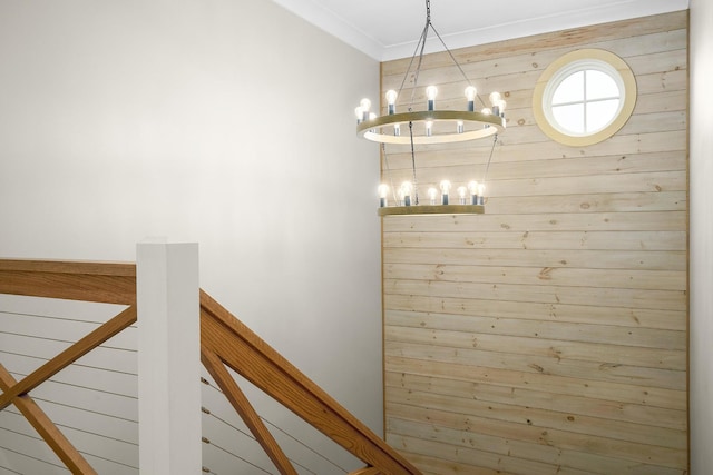 stairway with wooden walls, crown molding, and a chandelier