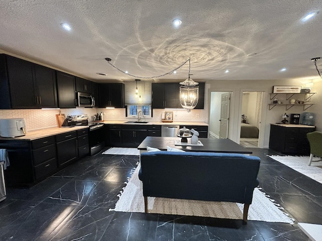 kitchen with appliances with stainless steel finishes, pendant lighting, decorative backsplash, sink, and an inviting chandelier