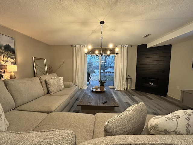 living room with a textured ceiling, a large fireplace, a notable chandelier, and dark wood-type flooring