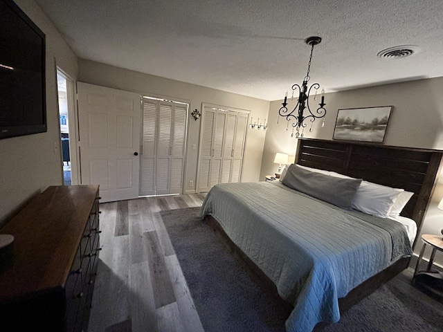 bedroom with two closets, a notable chandelier, a textured ceiling, and dark hardwood / wood-style floors