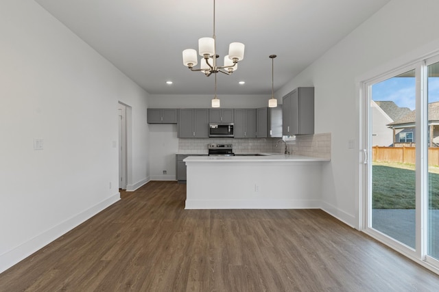 kitchen with an inviting chandelier, kitchen peninsula, gray cabinets, stainless steel appliances, and dark wood-type flooring