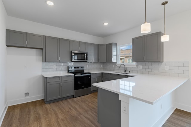 kitchen with kitchen peninsula, appliances with stainless steel finishes, decorative backsplash, decorative light fixtures, and sink