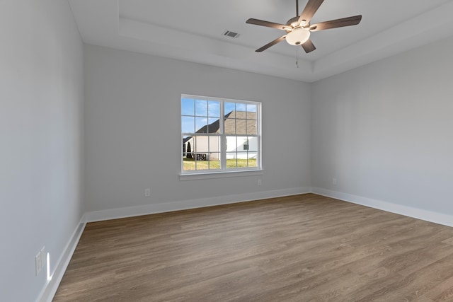 spare room with a raised ceiling, ceiling fan, and light hardwood / wood-style flooring