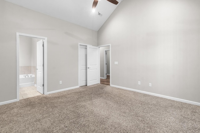 unfurnished bedroom with ceiling fan, light colored carpet, connected bathroom, and high vaulted ceiling