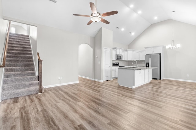 kitchen with stainless steel appliances, an island with sink, high vaulted ceiling, white cabinetry, and ceiling fan with notable chandelier