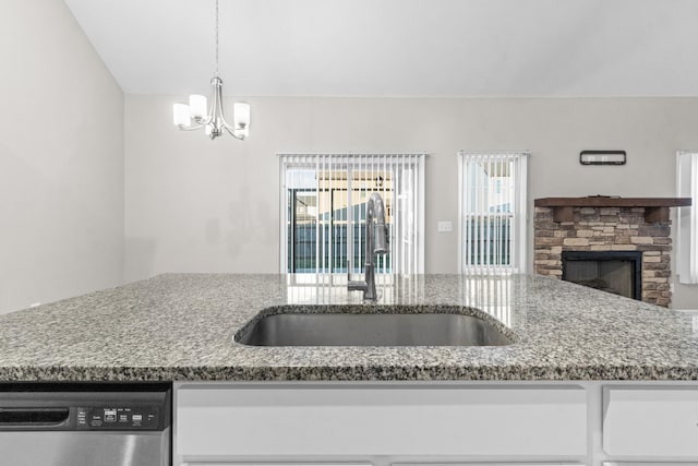 kitchen featuring stainless steel dishwasher, decorative light fixtures, sink, a notable chandelier, and a stone fireplace