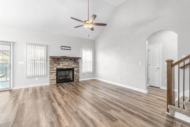 unfurnished living room with hardwood / wood-style flooring, high vaulted ceiling, ceiling fan, and a stone fireplace