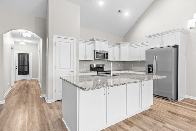 kitchen with light stone countertops, stainless steel appliances, high vaulted ceiling, white cabinetry, and sink