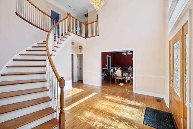 entryway featuring a towering ceiling, ornamental molding, a chandelier, and hardwood / wood-style floors