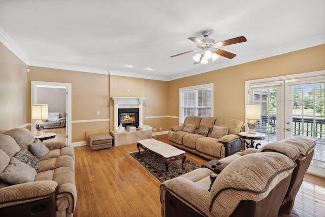 living room featuring light hardwood / wood-style floors, ceiling fan, crown molding, and a fireplace