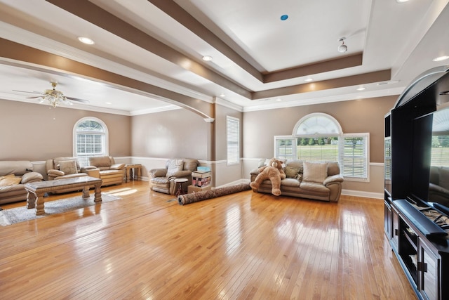 living room with a raised ceiling, light wood-type flooring, ceiling fan, and crown molding