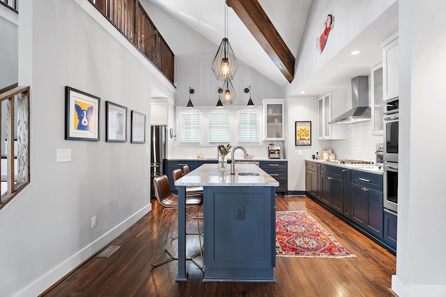 kitchen with white cabinetry, wall chimney range hood, decorative light fixtures, and a center island with sink