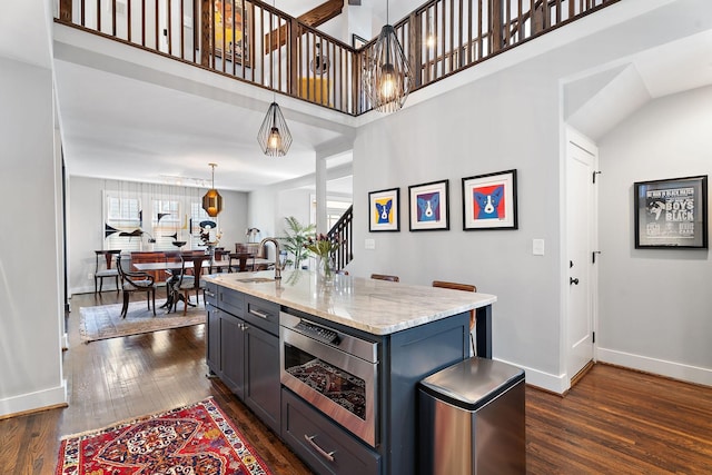 kitchen featuring light stone countertops, dark hardwood / wood-style floors, a high ceiling, hanging light fixtures, and a kitchen island with sink