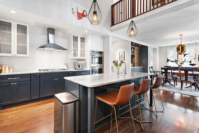 kitchen with a center island with sink, pendant lighting, wall chimney exhaust hood, white cabinets, and backsplash