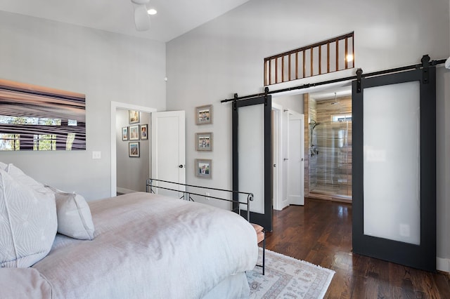 bedroom with ensuite bath, dark hardwood / wood-style floors, a towering ceiling, a barn door, and ceiling fan