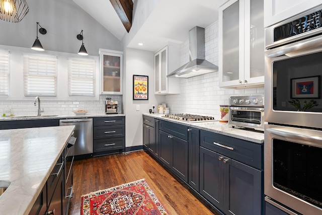 kitchen with hanging light fixtures, wall chimney range hood, white cabinetry, appliances with stainless steel finishes, and sink