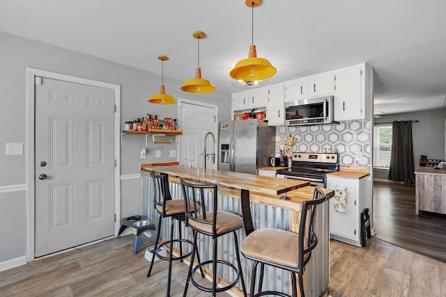 kitchen with stainless steel appliances, white cabinetry, light hardwood / wood-style flooring, wood counters, and hanging light fixtures