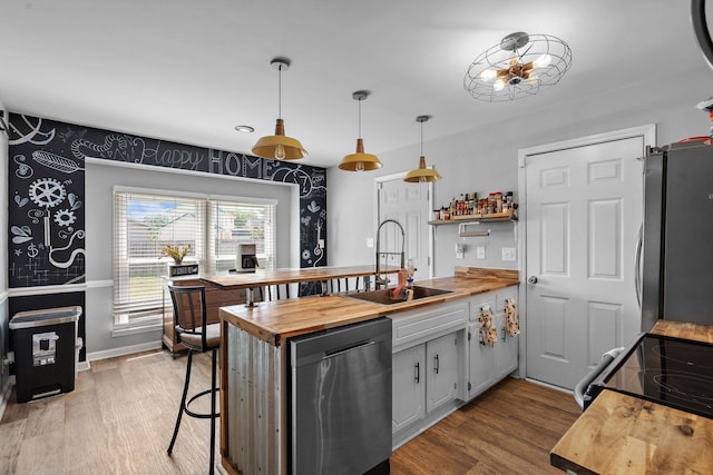 kitchen with stainless steel appliances, butcher block countertops, hardwood / wood-style flooring, sink, and decorative light fixtures