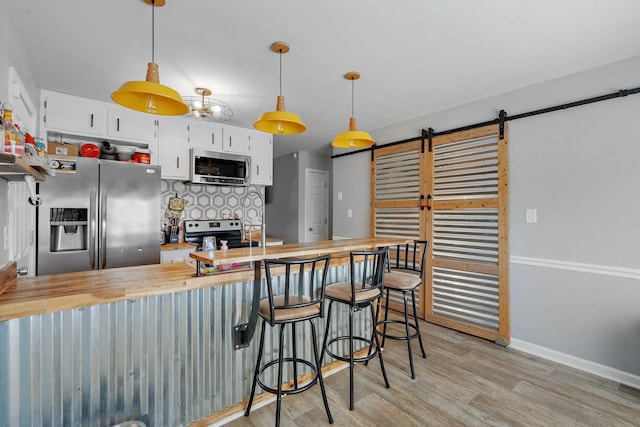 kitchen featuring stainless steel appliances, decorative light fixtures, white cabinetry, wood counters, and a barn door