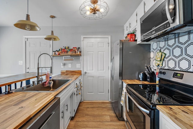 kitchen featuring hanging light fixtures, wood counters, white cabinetry, appliances with stainless steel finishes, and sink