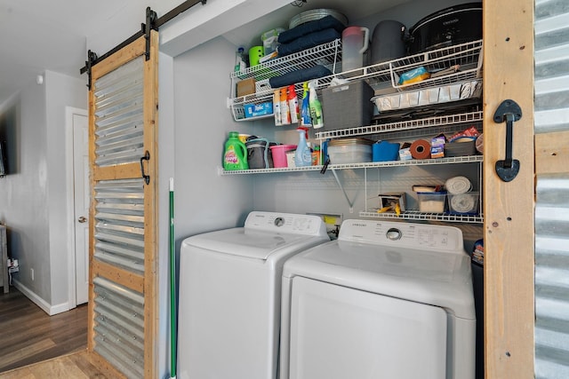 clothes washing area with separate washer and dryer, a barn door, and hardwood / wood-style flooring