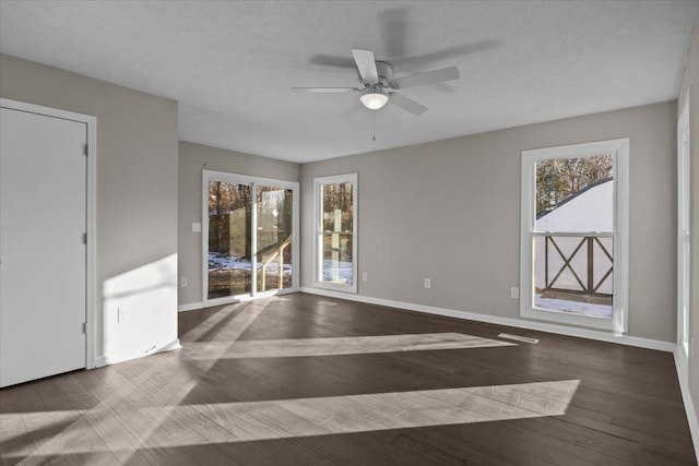 unfurnished room featuring a healthy amount of sunlight, ceiling fan, and dark wood-type flooring