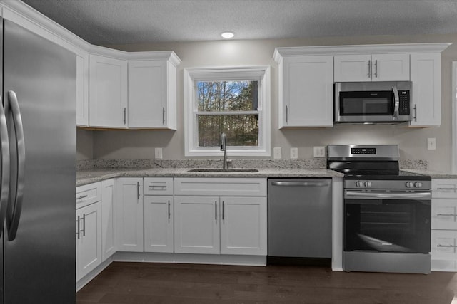 kitchen featuring light stone countertops, a textured ceiling, stainless steel appliances, white cabinetry, and sink