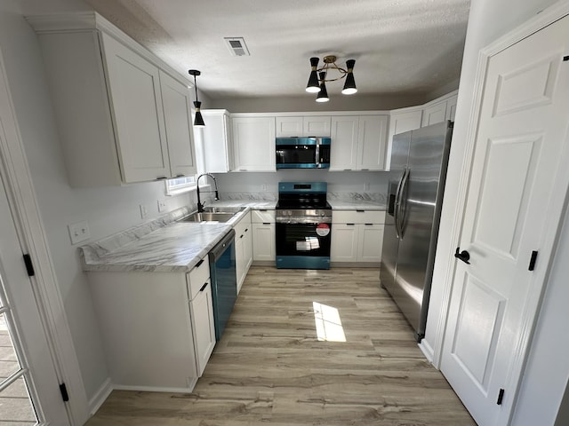 kitchen featuring appliances with stainless steel finishes, hanging light fixtures, sink, light hardwood / wood-style flooring, and white cabinetry