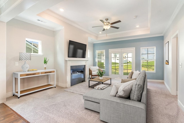 living room featuring a raised ceiling, ceiling fan, light carpet, and ornamental molding