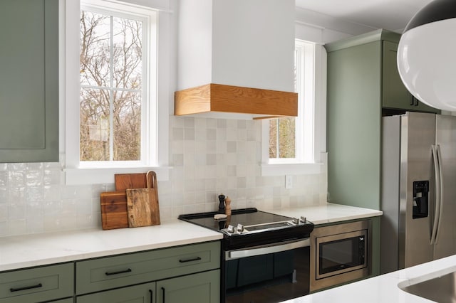 kitchen featuring stainless steel appliances, green cabinets, tasteful backsplash, and premium range hood