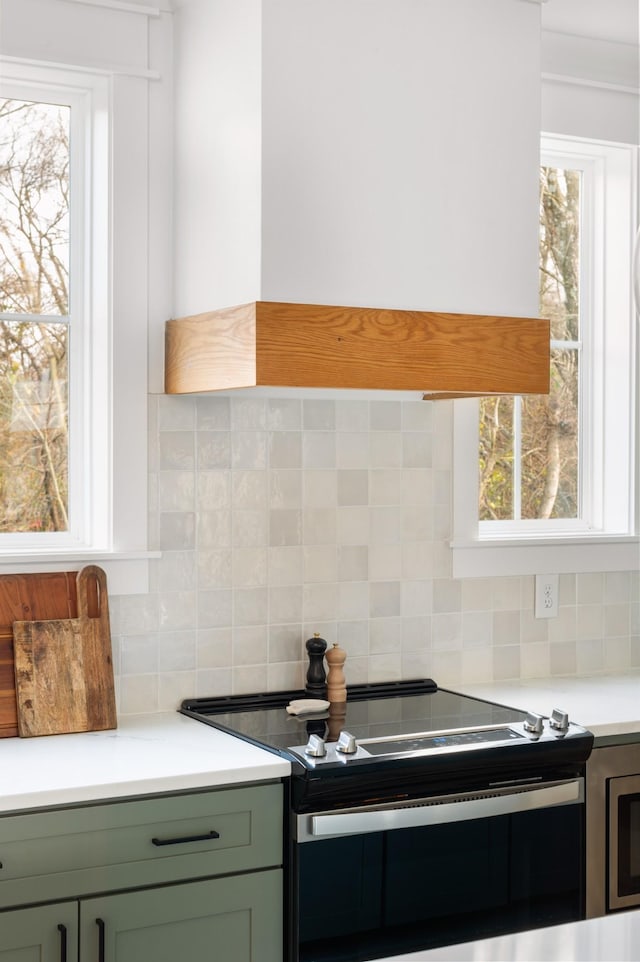 kitchen with stainless steel electric range oven, custom exhaust hood, tasteful backsplash, and green cabinets