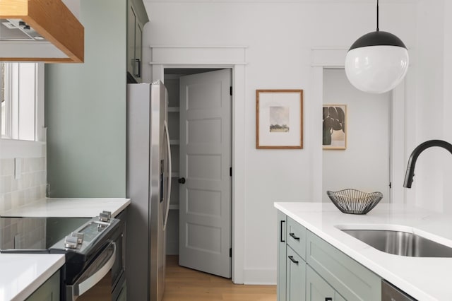 kitchen with decorative light fixtures, stainless steel appliances, tasteful backsplash, light wood-type flooring, and sink