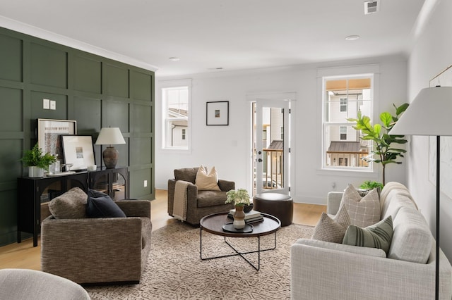 living room featuring light wood-type flooring, crown molding, and plenty of natural light