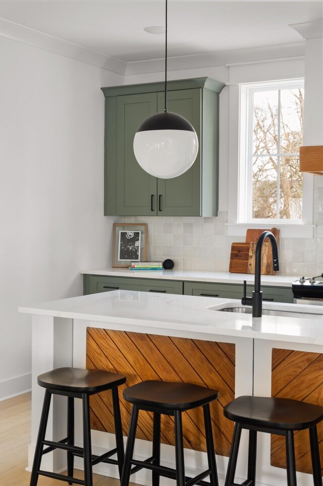 bar featuring hanging light fixtures, green cabinetry, tasteful backsplash, light wood-type flooring, and sink