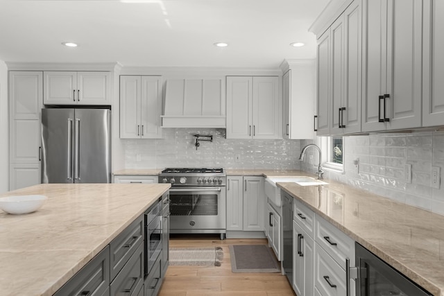 kitchen with beverage cooler, premium appliances, light stone counters, and light hardwood / wood-style flooring