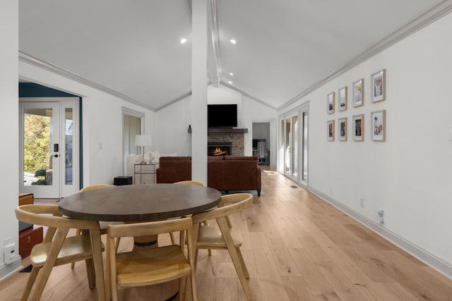 dining room featuring a fireplace, light hardwood / wood-style floors, ornamental molding, and vaulted ceiling with beams