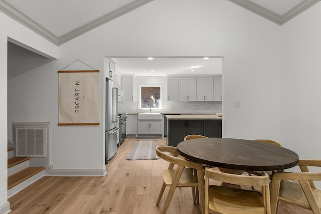 dining room with sink, ornamental molding, vaulted ceiling, and light hardwood / wood-style flooring