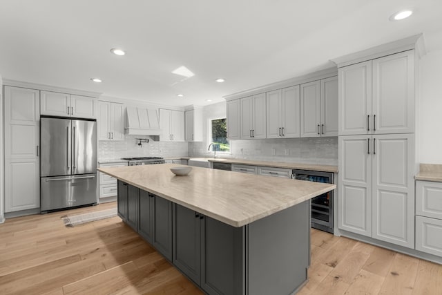 kitchen featuring custom exhaust hood, beverage cooler, stainless steel refrigerator, light hardwood / wood-style floors, and a kitchen island