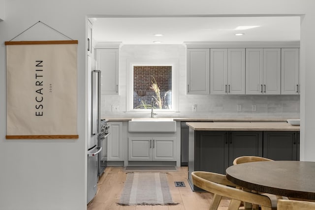 kitchen with tasteful backsplash, stainless steel range, light wood-type flooring, gray cabinets, and sink