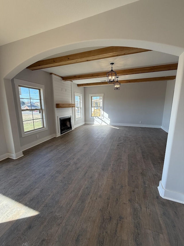 unfurnished living room featuring a fireplace, dark hardwood / wood-style floors, a healthy amount of sunlight, and beam ceiling