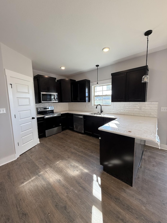 kitchen with stainless steel appliances, hanging light fixtures, kitchen peninsula, dark hardwood / wood-style floors, and backsplash